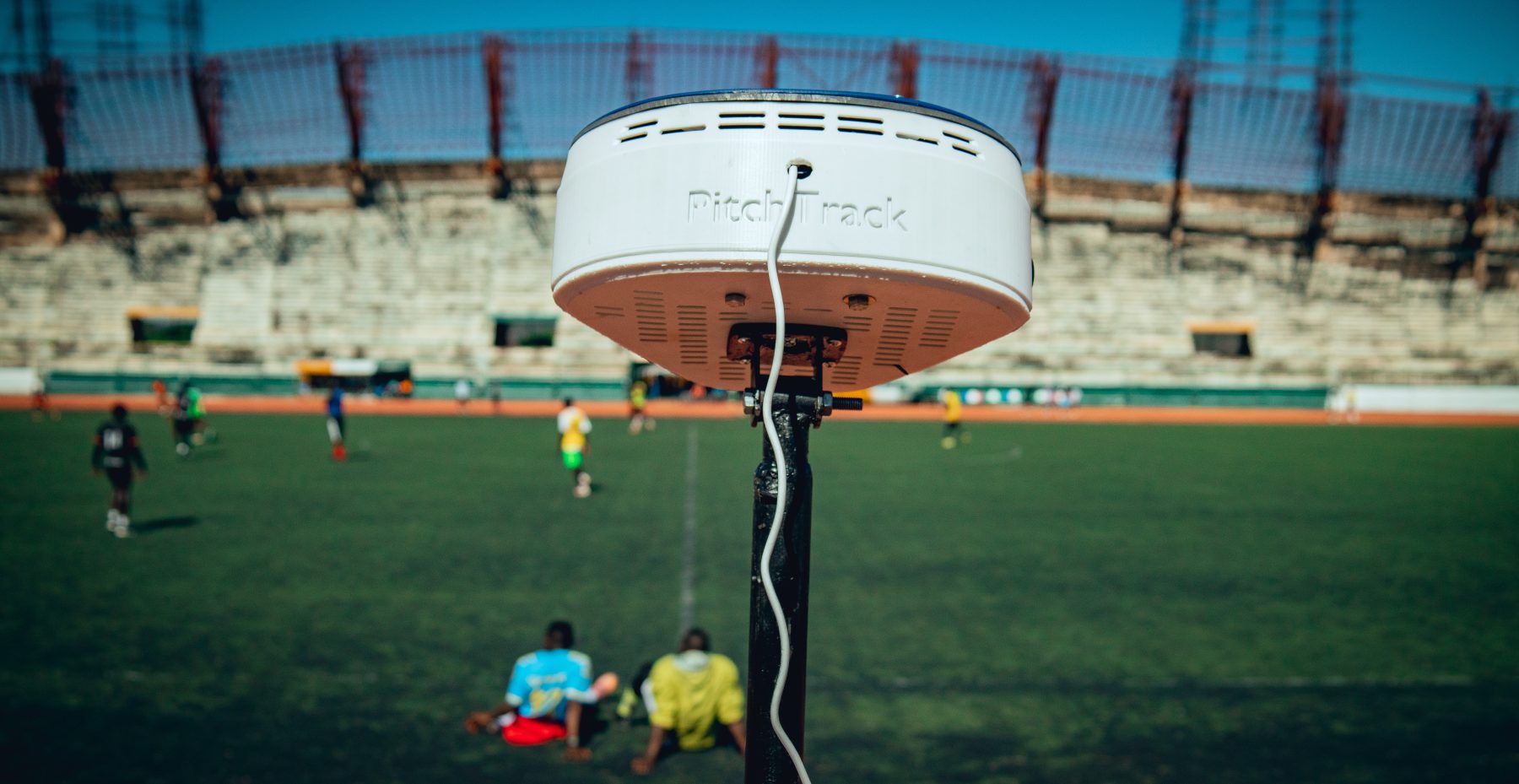 The PitchTrack head mounted on a mast at the edge of a football pitch, with a match being played behind it.